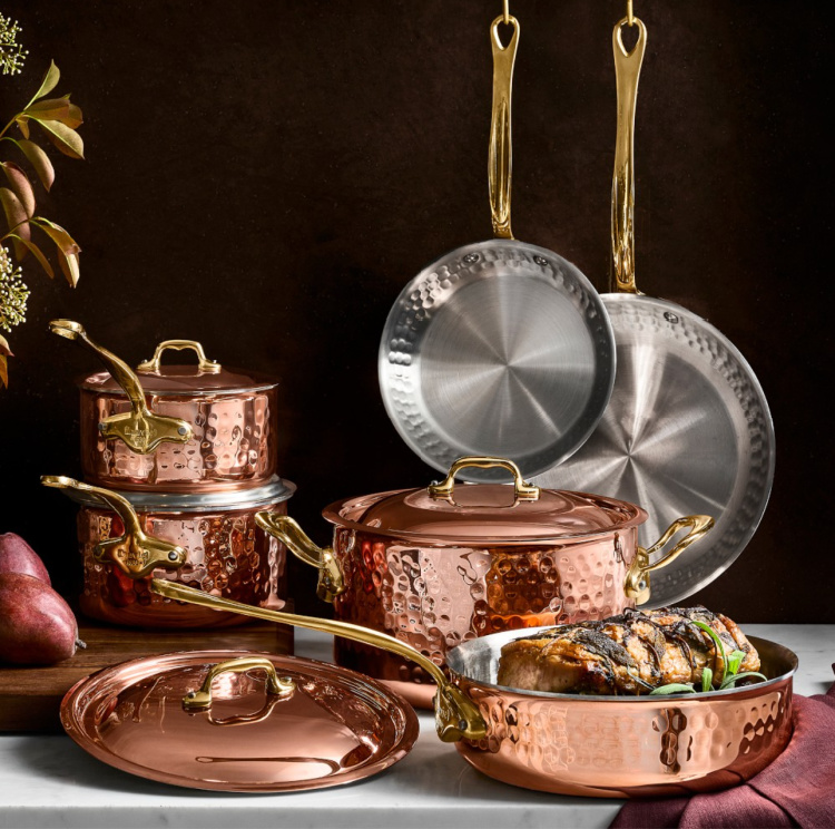 Hammered copper pots and pans with gold-toned handles, displayed with matching lids and a roast in a sauté pan.