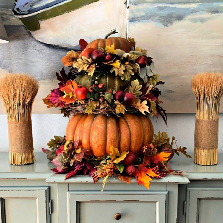 Faux pumpkins stacked with decorated grapevine wreaths to create a fall display.